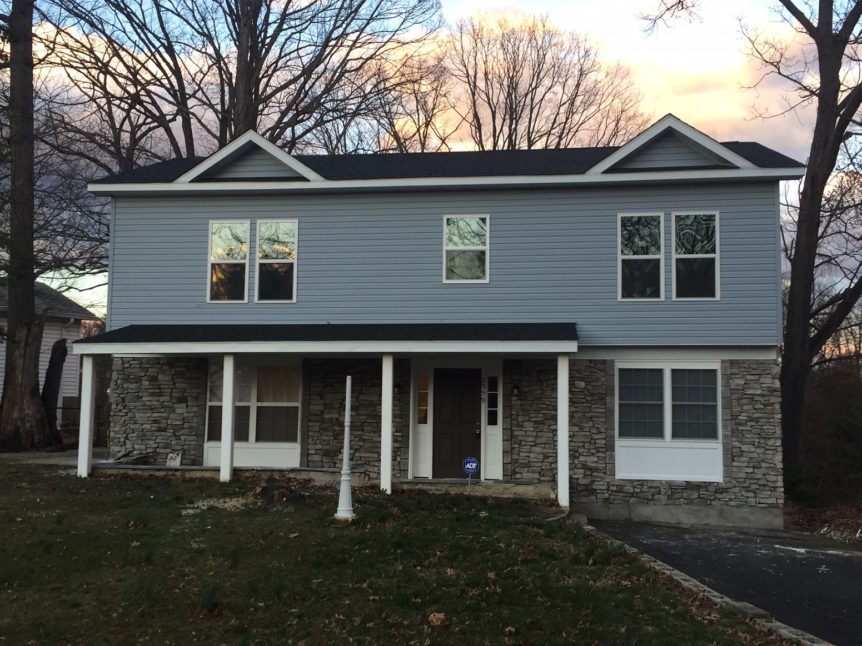 Two story home with stones decorating first floor and blue siding on the second floor