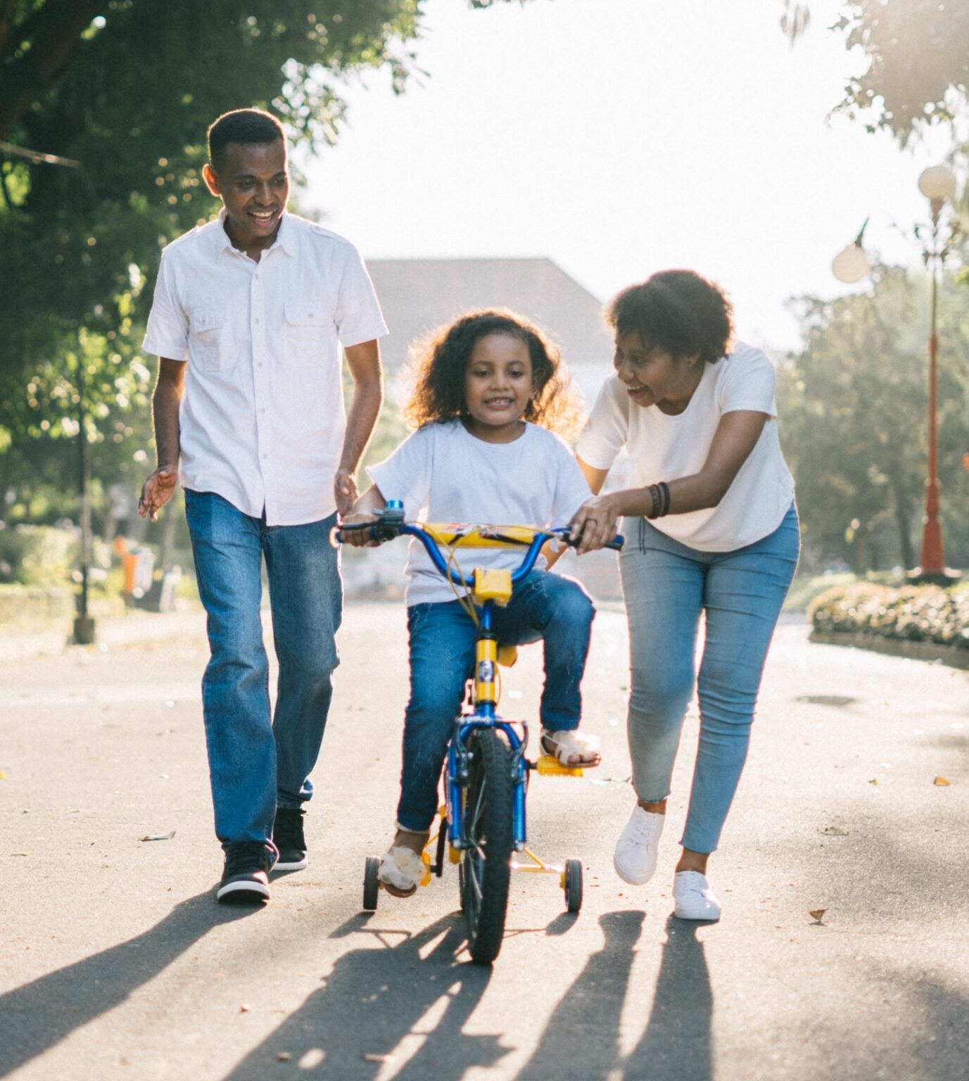 A Black mom and dad are teaching their child to ride a bike in a residential area
