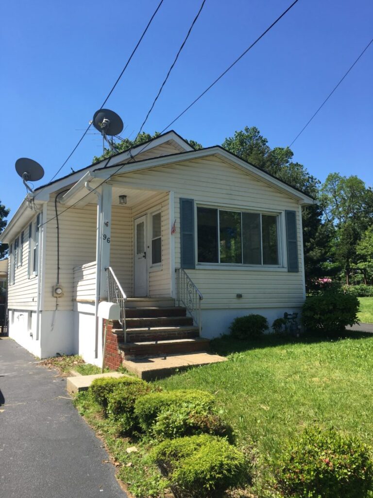 A deep house with wide front window and lawn and a driveway to the left