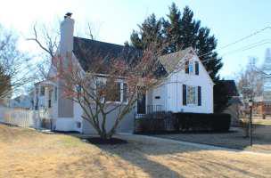 White home with a chimney and a bare tree in front, a fir tree in back