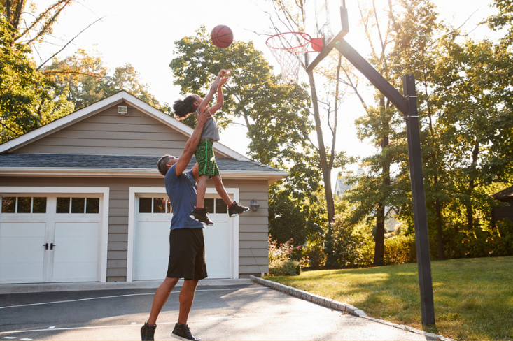 Father and daughter on their driveway playing basketball in front of their garage