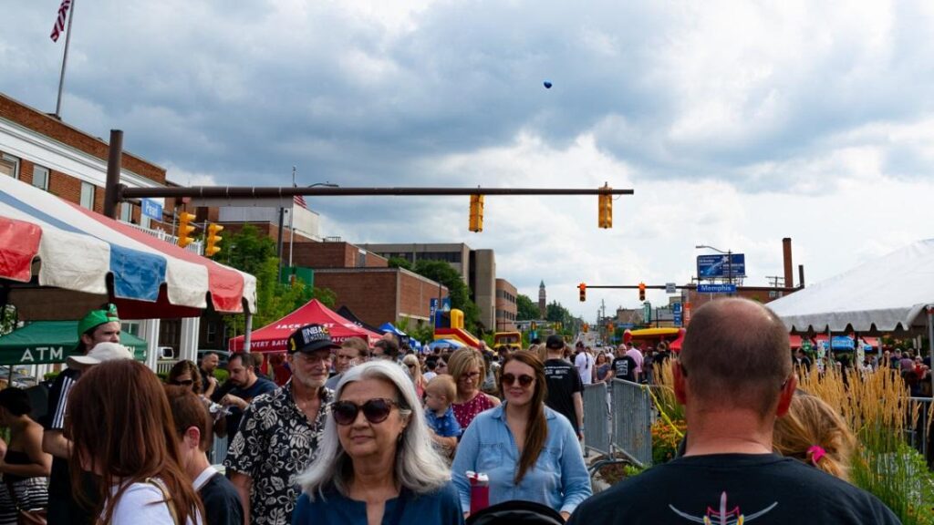 A crowd moving through a street festival on a cloudy day